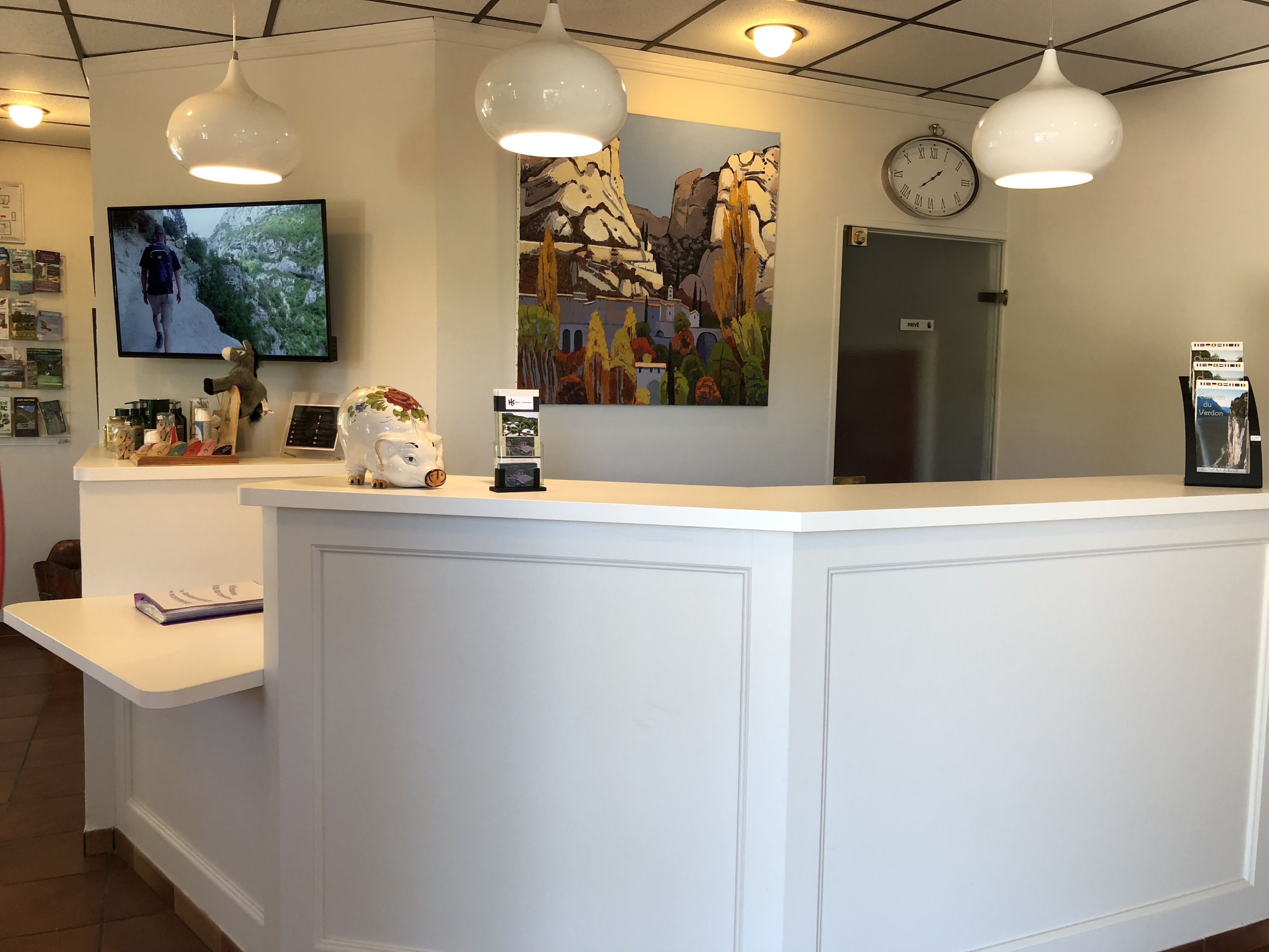 A reception desk with a mounted television, a clock, and a painting of a mountainous landscape.