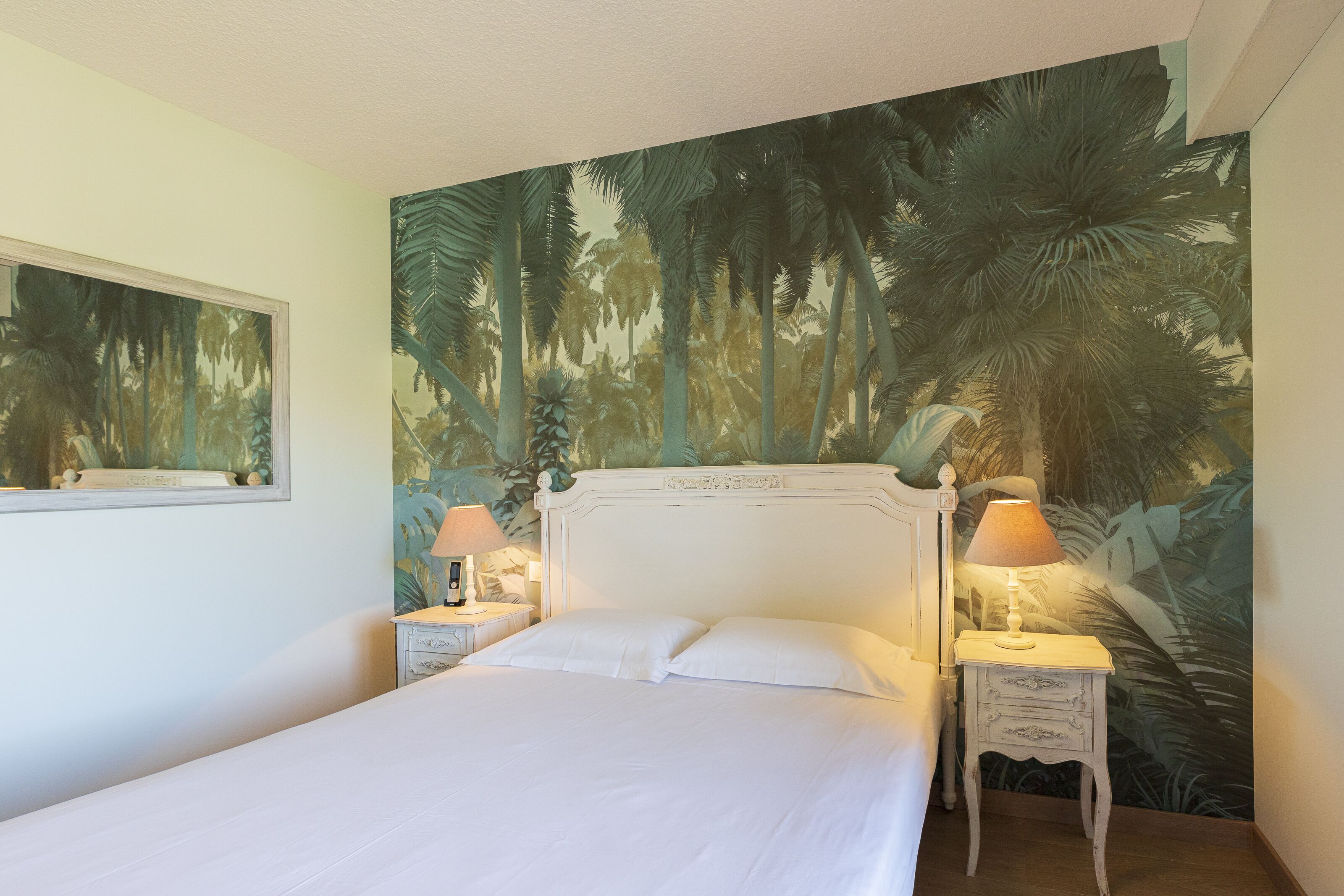 A bedroom with a bed, two bedside tables, and a large tropical mural on the wall.