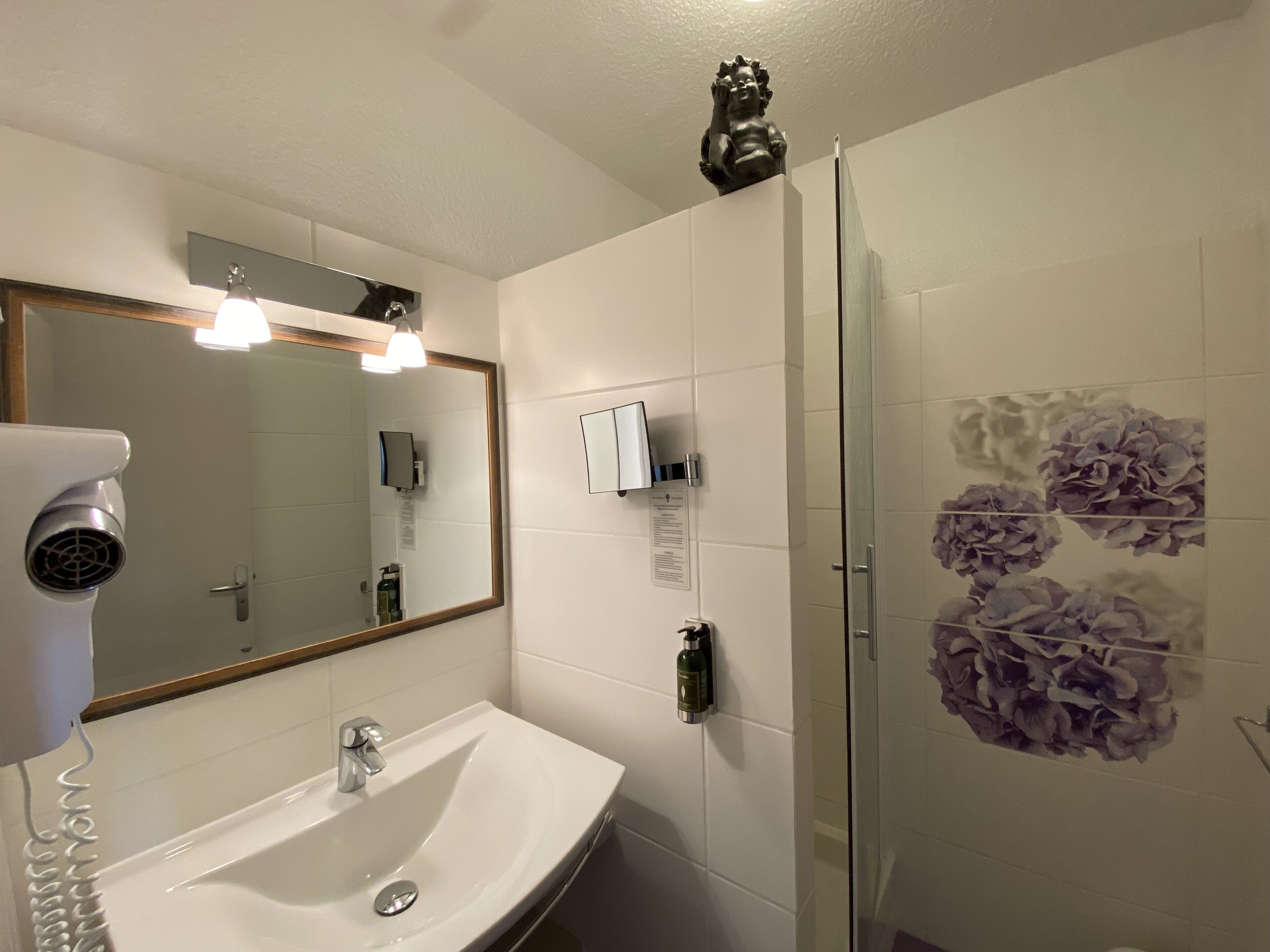 A bathroom with a white sink, a large mirror, a hairdryer, and a glass shower enclosure.