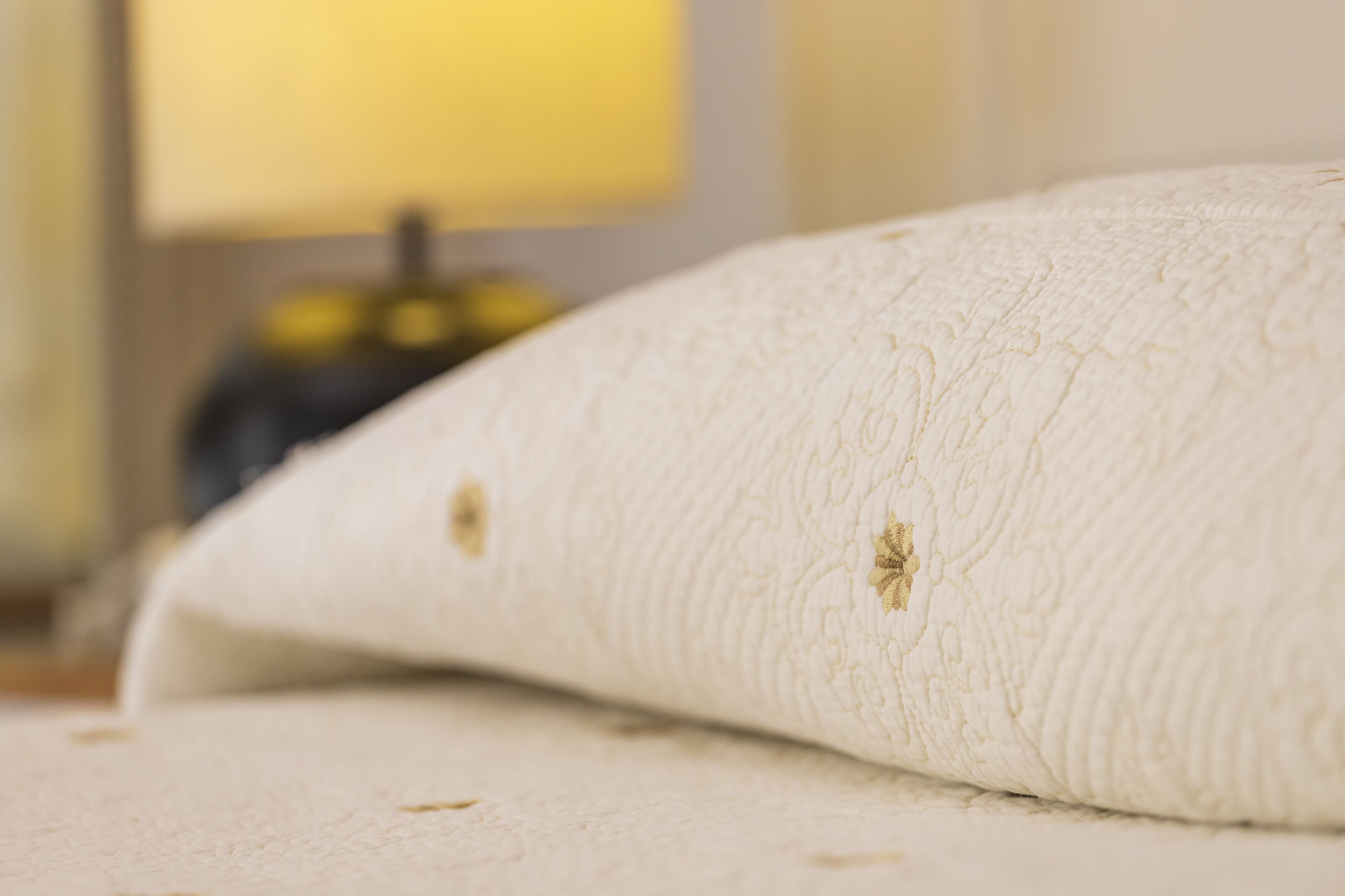 Un gros plan d’un coussin blanc à la texture particulière, orné d’un motif discret, posé sur une surface dont l’arrière-plan est flou.