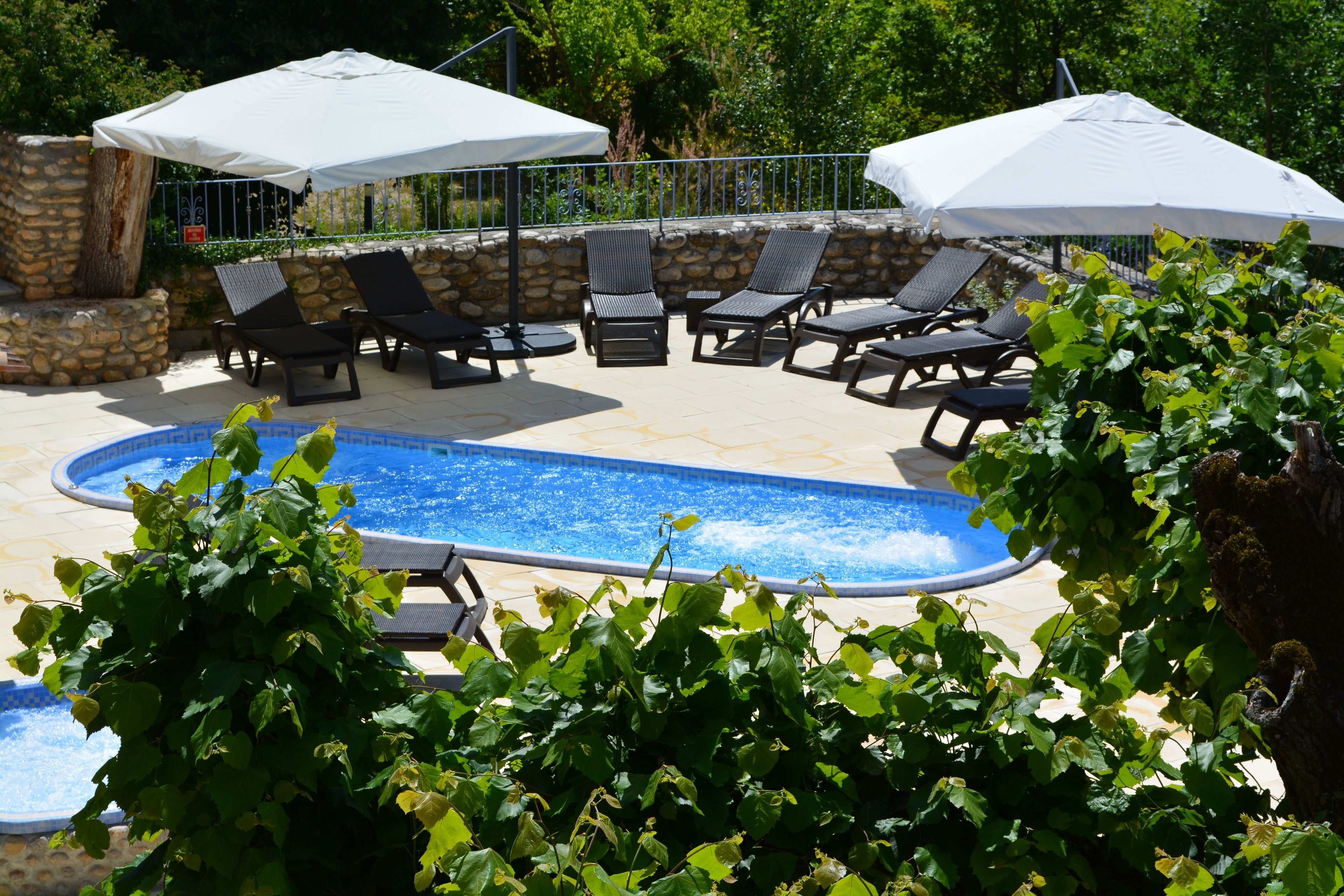 Un espace aménagé au bord de la piscine, avec des chaises longues et des parasols, entouré de murs en pierre et de verdure.