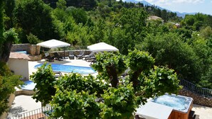 A pool area with lounge chairs and umbrellas, surrounded by lush greenery and mountains in the background. - Hôtel Le Colombier (Moustiers-Sainte-Marie)