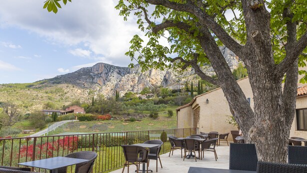 An outdoor patio with wicker furniture and a view of a mountainous landscape. - Hôtel Le Colombier (Moustiers-Sainte-Marie)