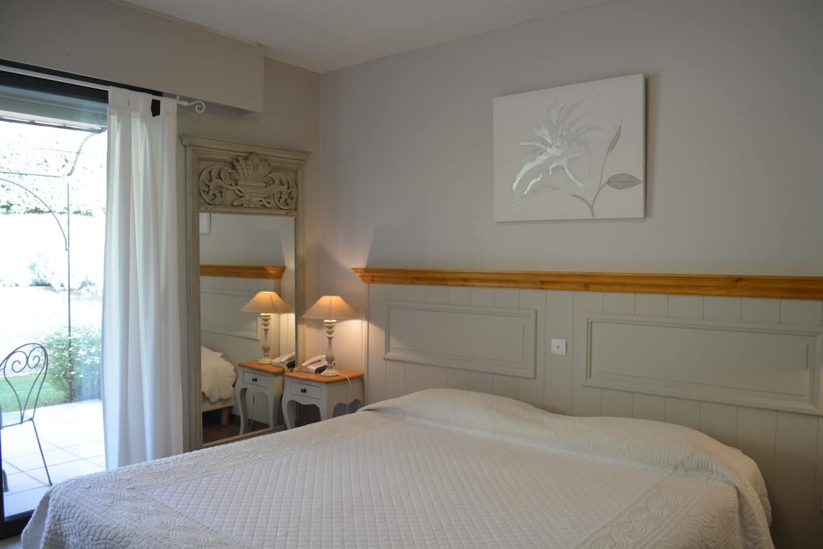 A bedroom with a bed, bedside lamps, a mirror, and a framed floral artwork on the wall.
