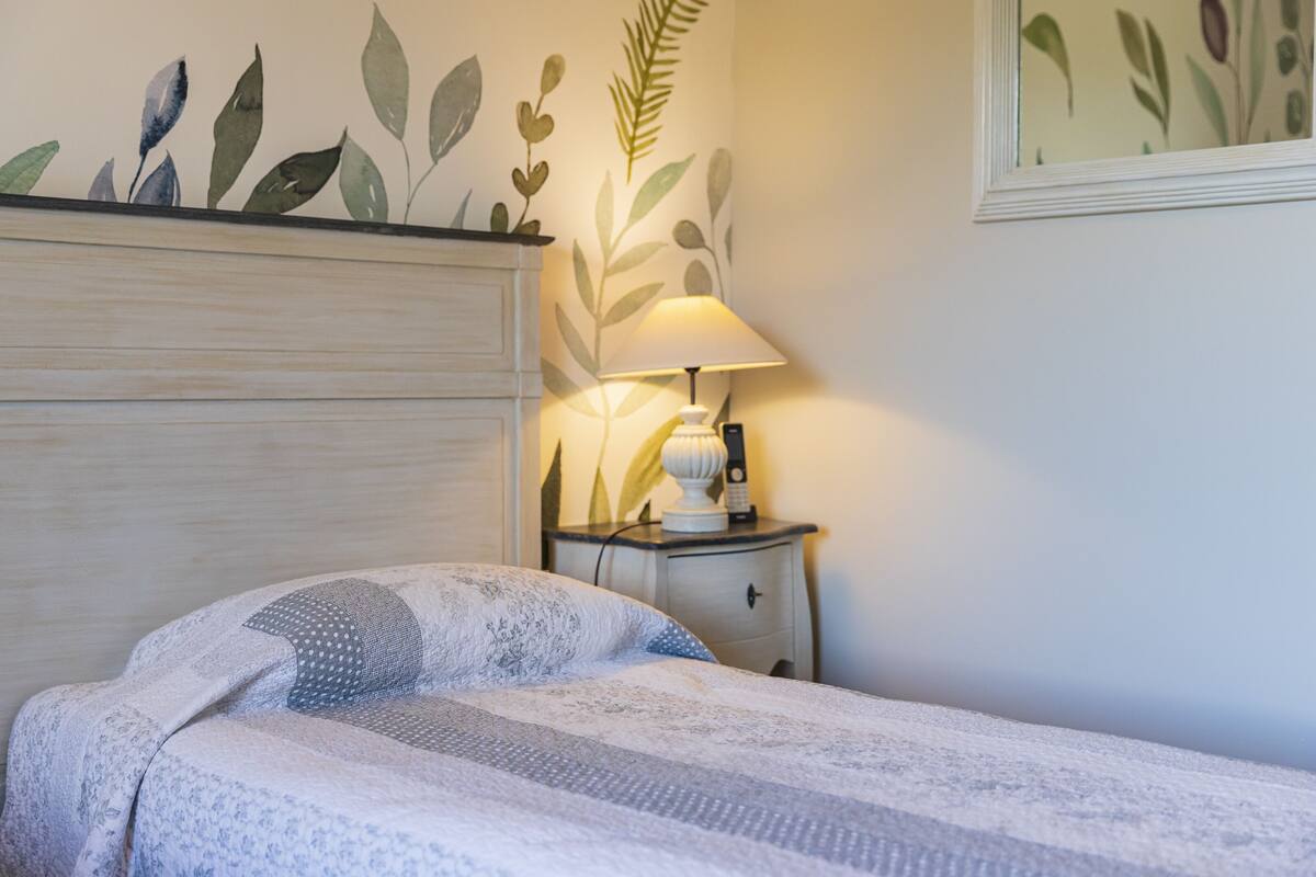 A neatly made bed with a patterned bedspread, a bedside lamp, and a nightstand with a phone and a lamp.