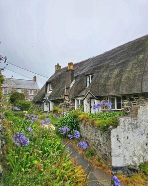 A row of traditional stone houses with thatched roofs, surrounded by lush gardens and flowering plants.