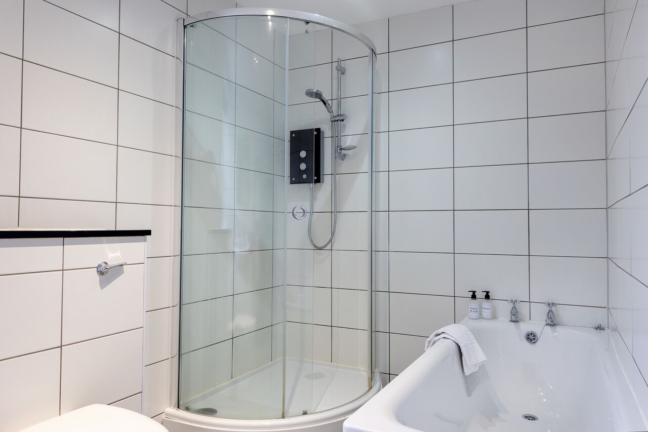 A modern bathroom with a glass-enclosed shower, a white bathtub, and tiled walls.
