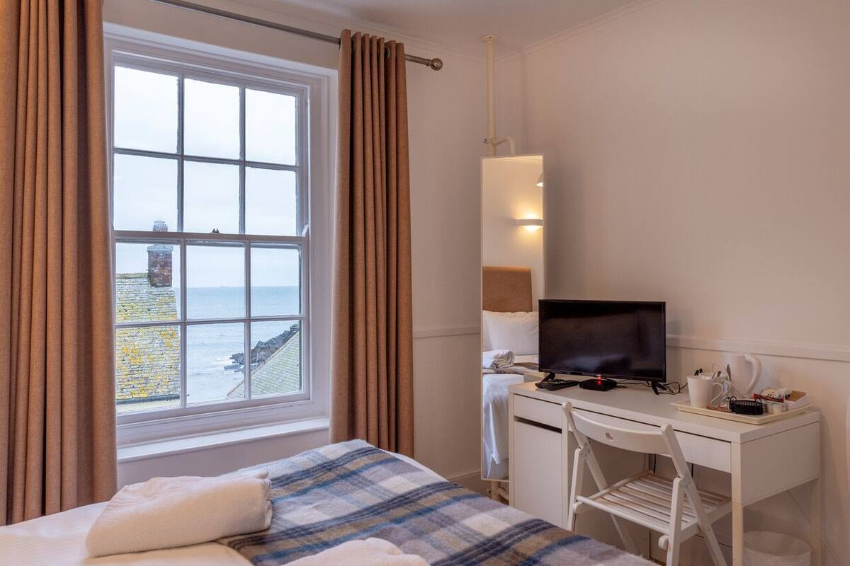 A hotel room with a bed, a desk with a computer, a TV, and a view of the sea through a window.
