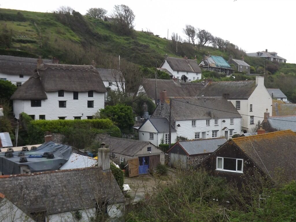 A cluster of white houses with thatched roofs, surrounded by greenery and hills.