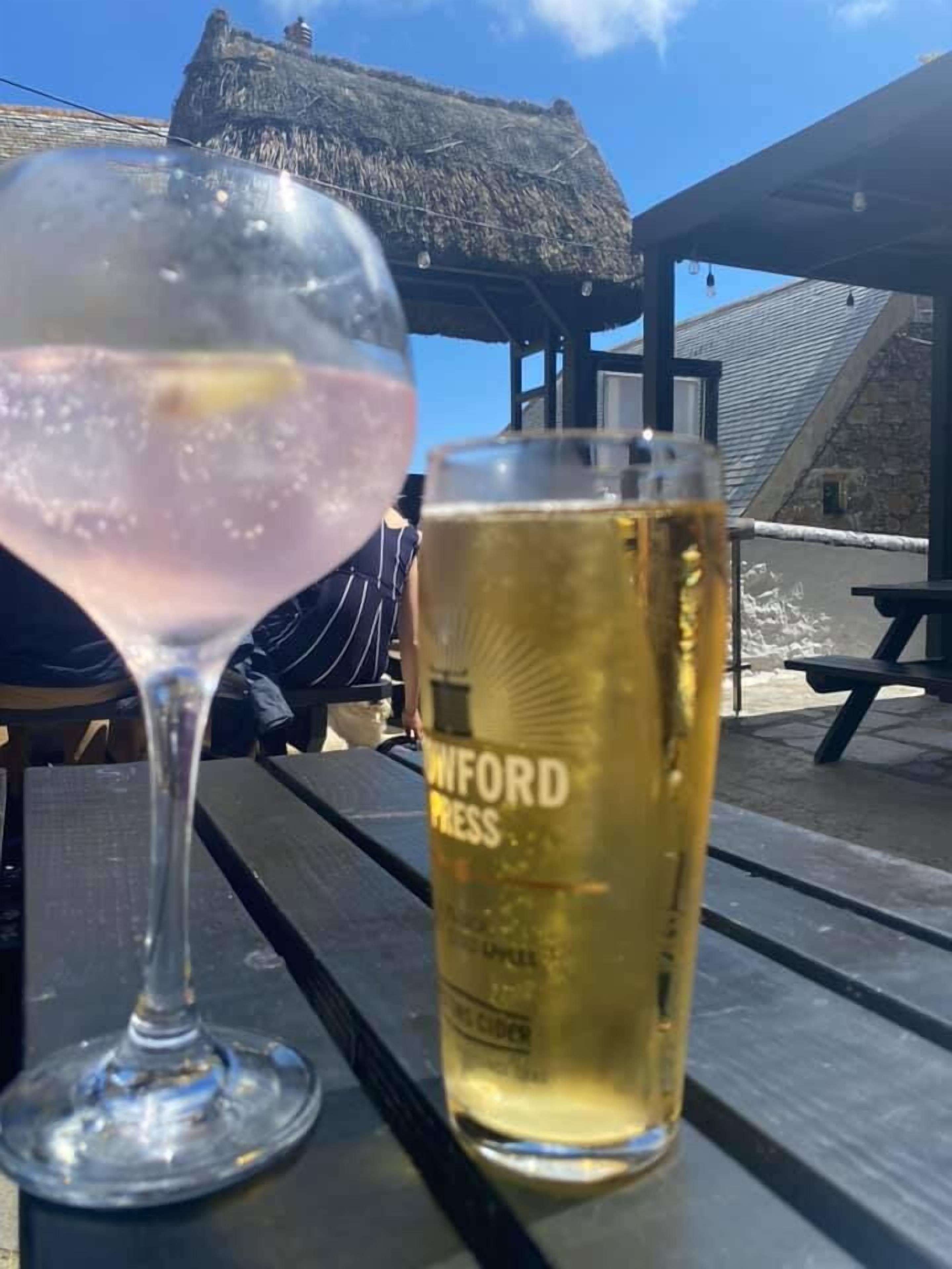 A glass of a pink cocktail and a can of cider on a wooden table.