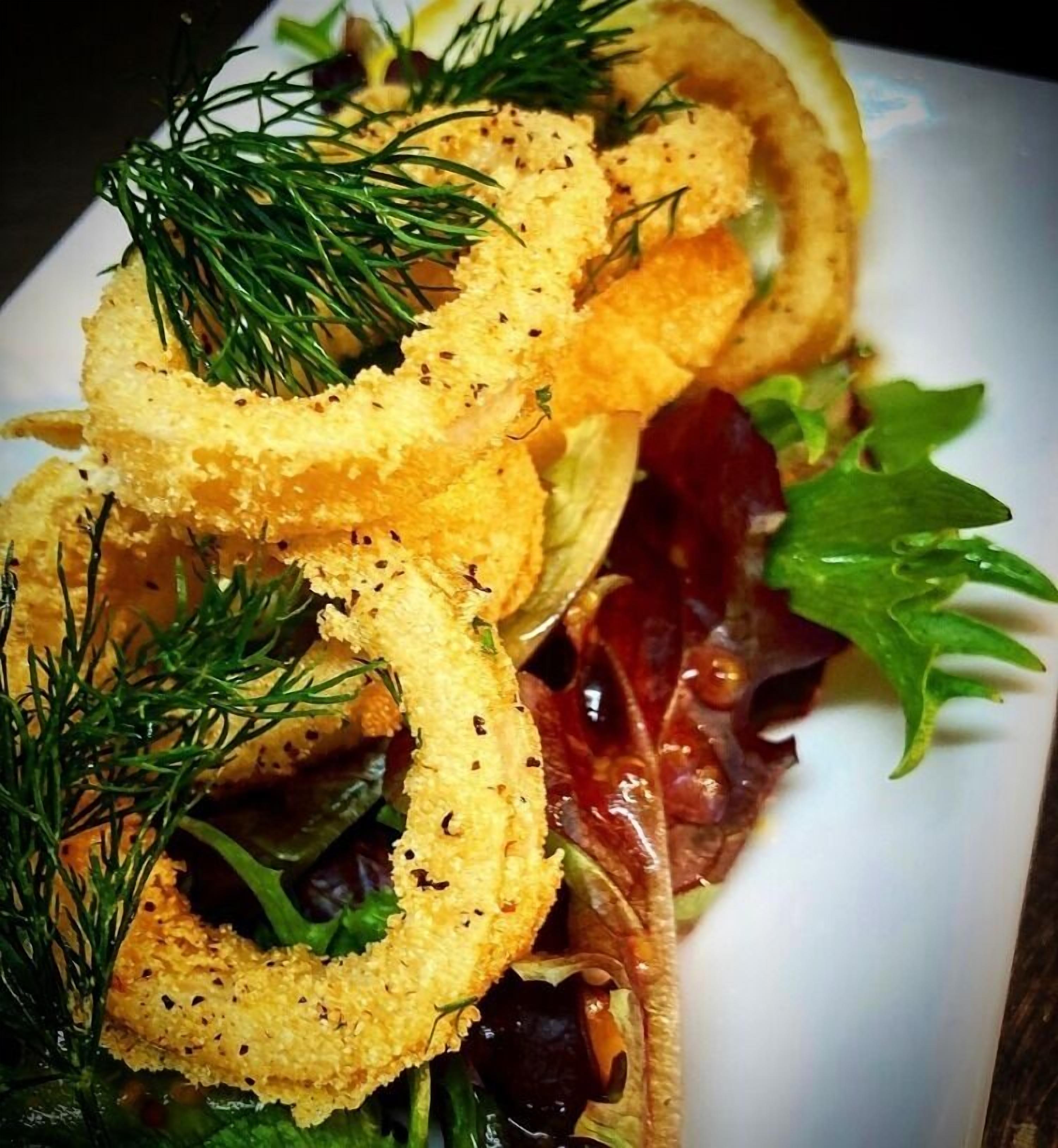 Une assiette de rondelles de calamars frits, de légumes frais et d’un quartier de citron.
