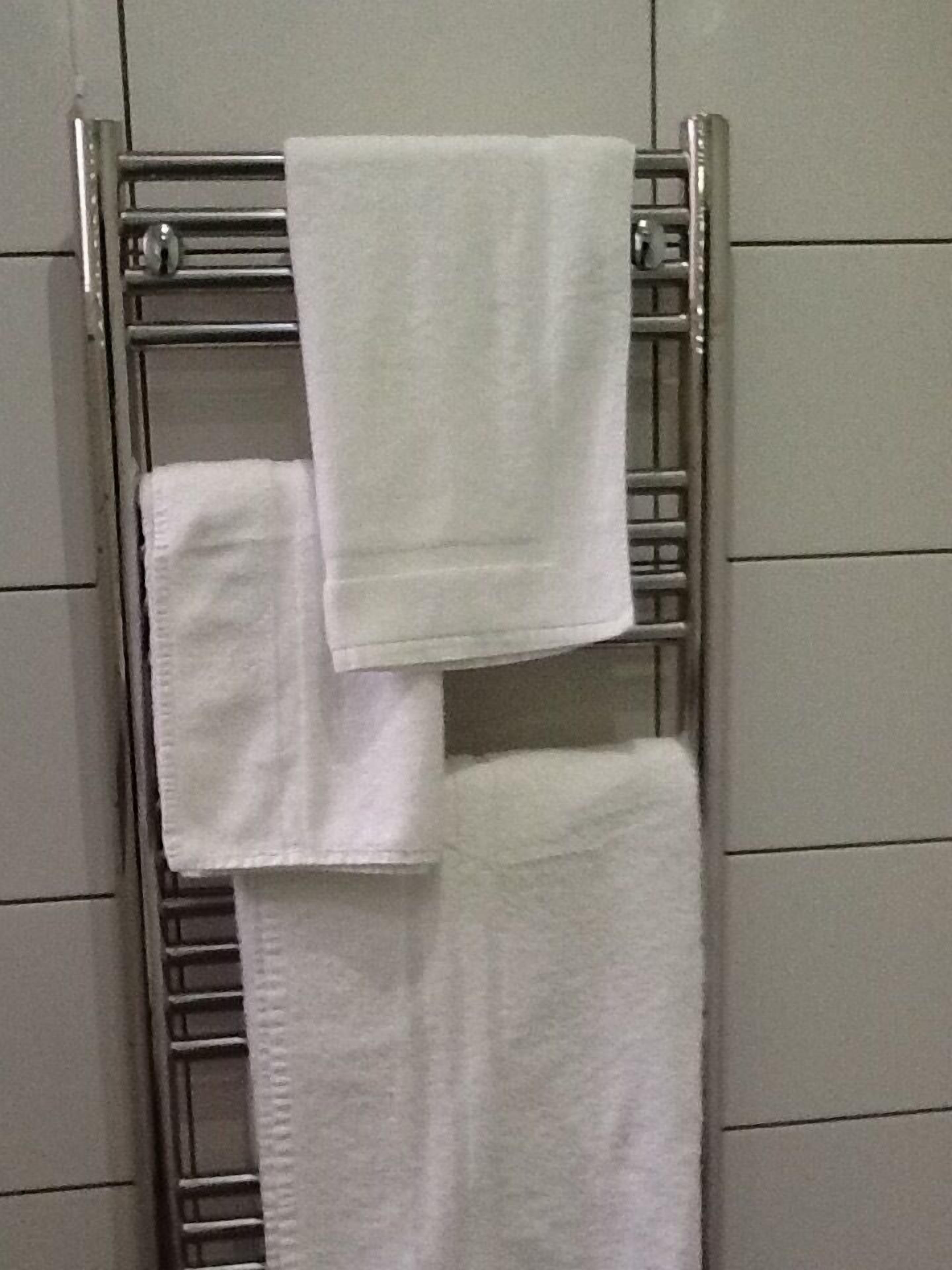 A metal towel rack with three white towels hanging.