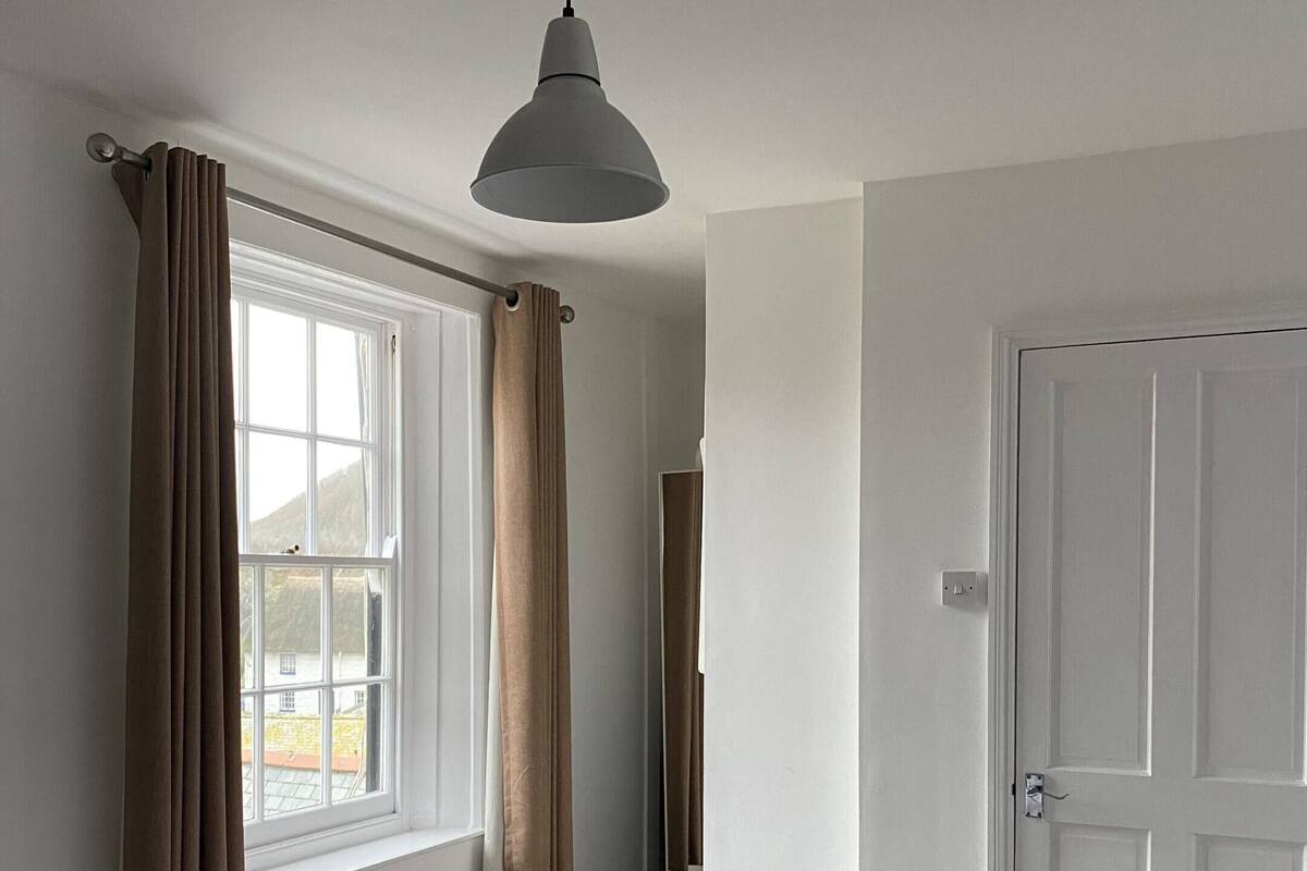 A bedroom with a bed, a window with curtains, a door, and a ceiling light fixture.