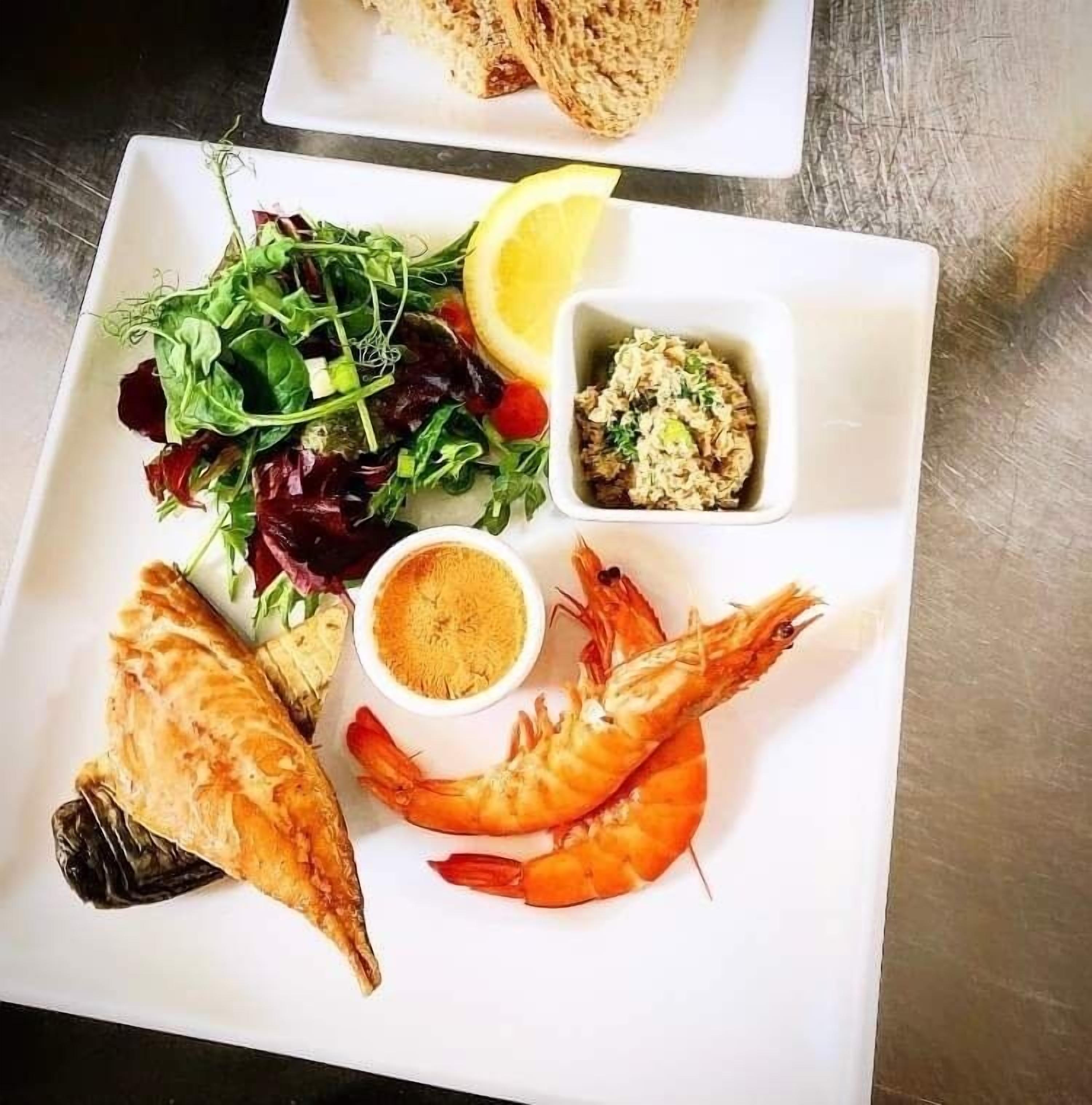 Un plato con pescado a la parrilla, camarones, una ensalada y un gajo de limón.
