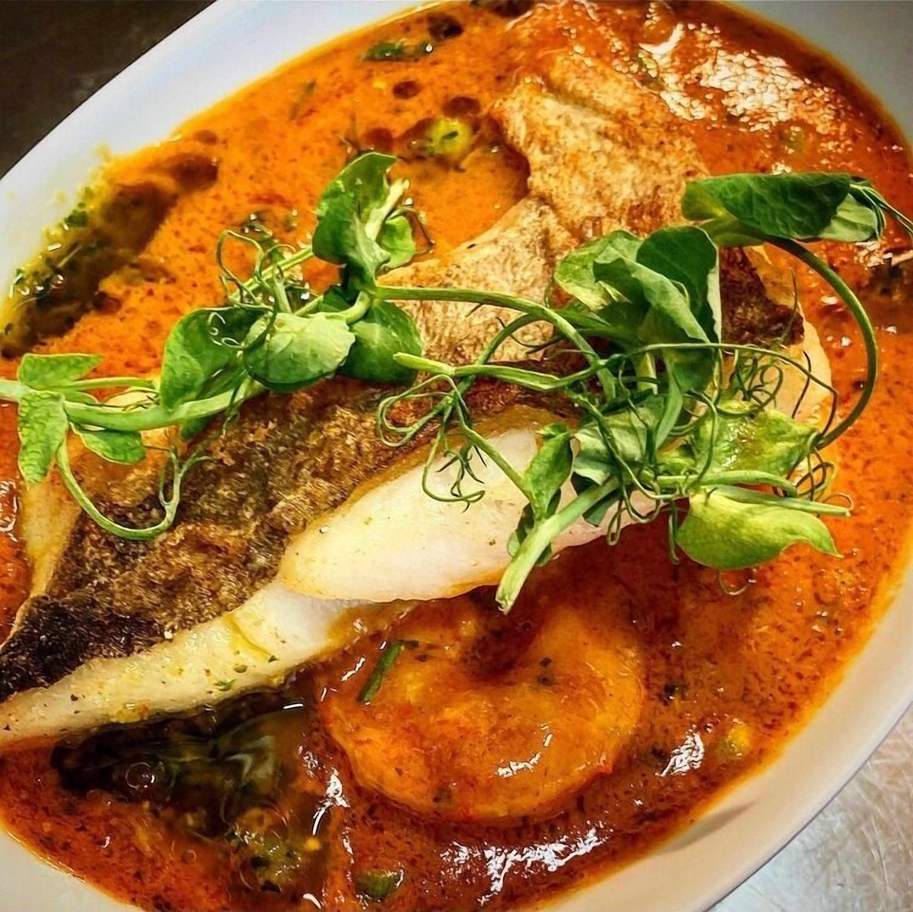 A dish with fish, vegetables, and herbs in a broth.