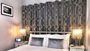 Una cama bien hecha con cubrecama acolchada, dos mesitas de noche con lámparas, un cuadro colgado en la pared y una cortina estampada.