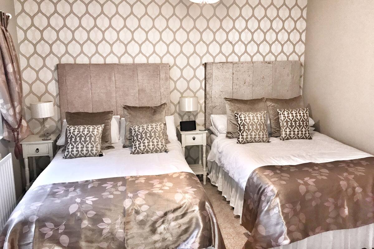 Une chambre d’hôtel avec deux lits, un mur orné de motifs et un lustre.