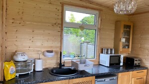 Una cocina compacta con paredes de madera, una ventana, microondas, tostadora y pileta.
