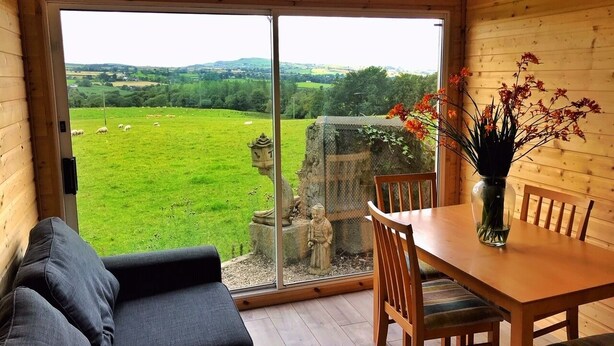 Una habitación con un gran ventanal corredera que da a un campo cubierto de hierba, una mesa de comedor de madera con sillas y un sofá.