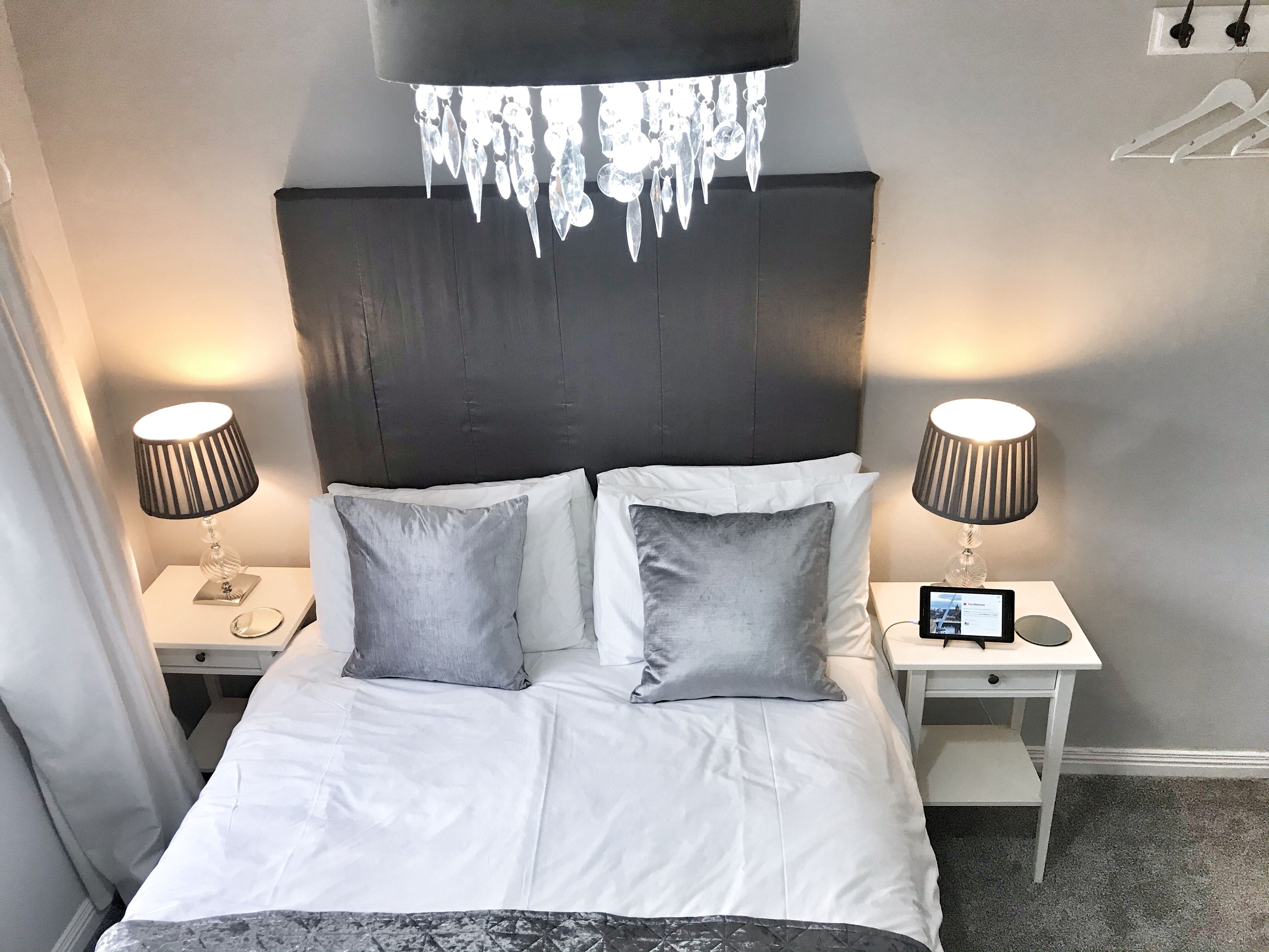 A hotel room with a bed, two bedside tables, a chandelier, and a tablet on one of the tables.