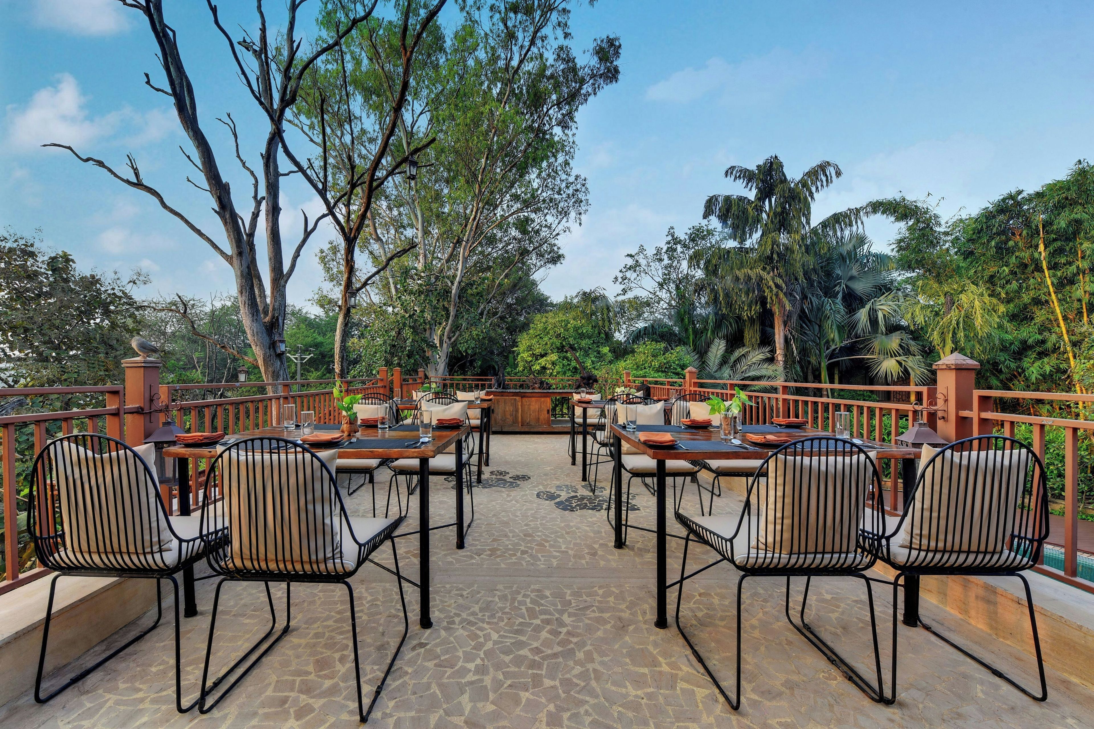 An outdoor dining area with tables and chairs, surrounded by trees and a wooden fence.
