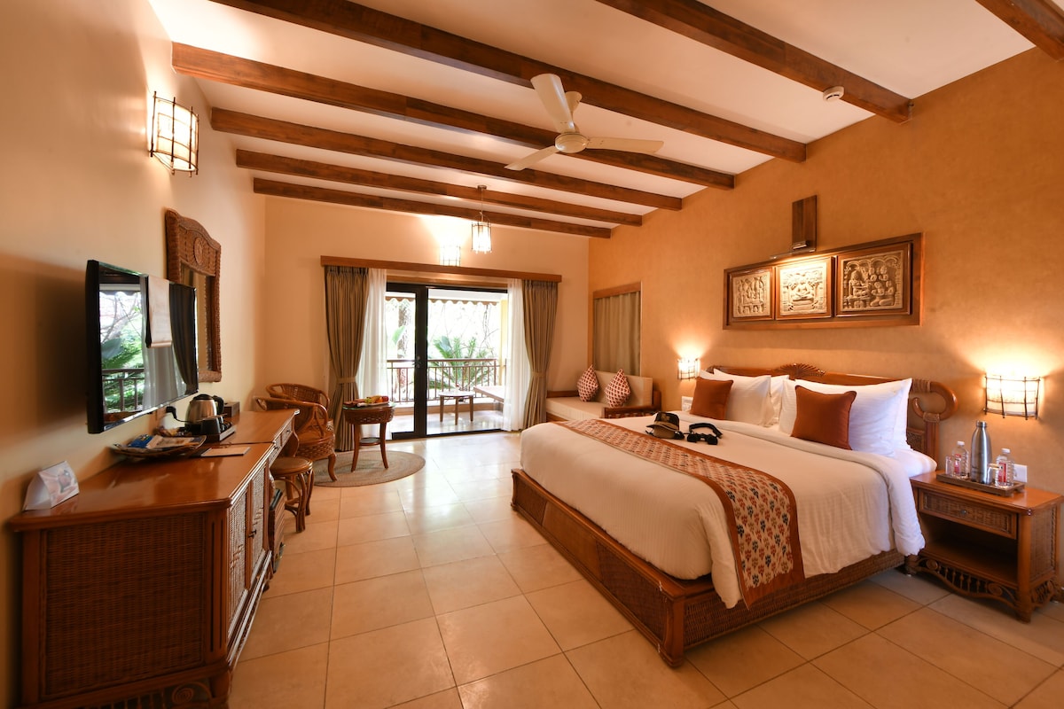 A spacious bedroom with a large bed, wooden ceiling beams, a ceiling fan, and a view to the outside.