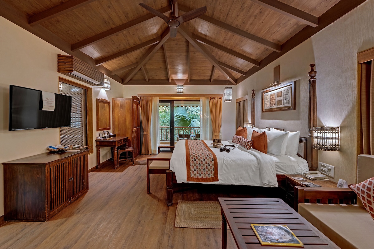 A spacious bedroom with a large bed, wooden ceiling beams, a desk, and a television.
