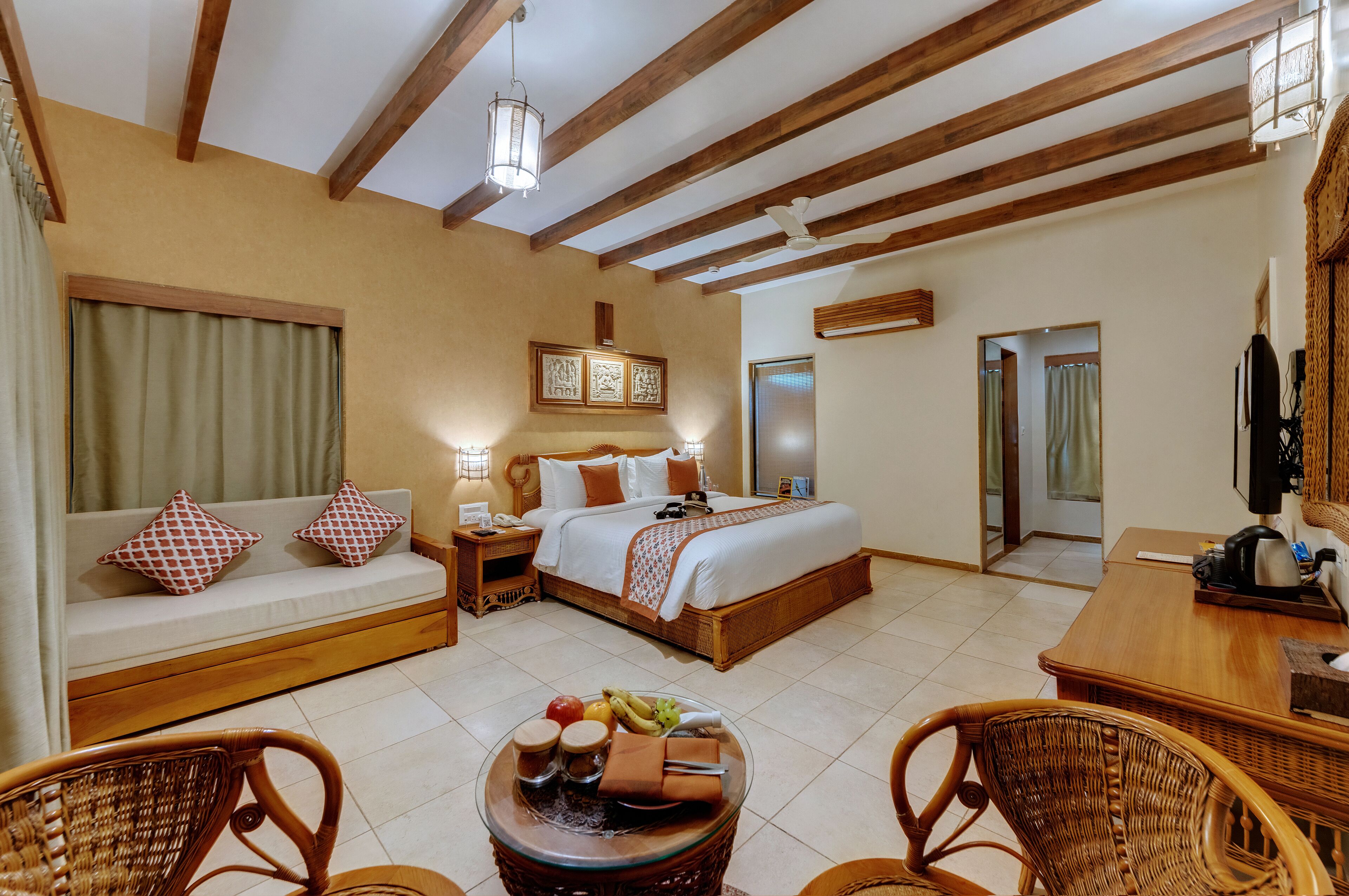 Une chambre d’hôtel comprenant un lit, un canapé, une table à manger, des chaises en osier et un panier de fruits.