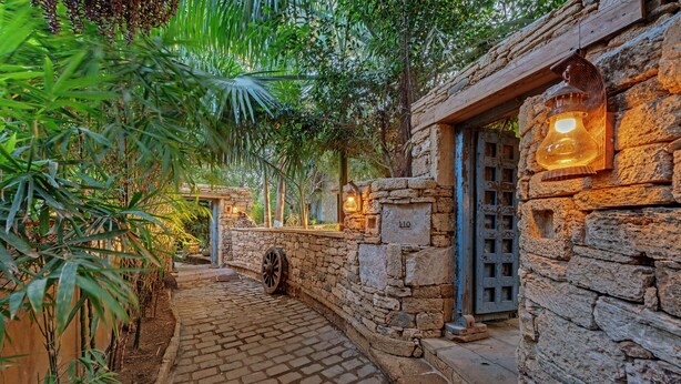 Un sentier pavé de pierres menant à un bâtiment rustique en pierre, orné d’une lanterne et doté d’une porte.