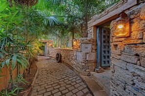 Un sendero empedrado que conduce a un rústico edificio de piedra con un farol y una puerta.
