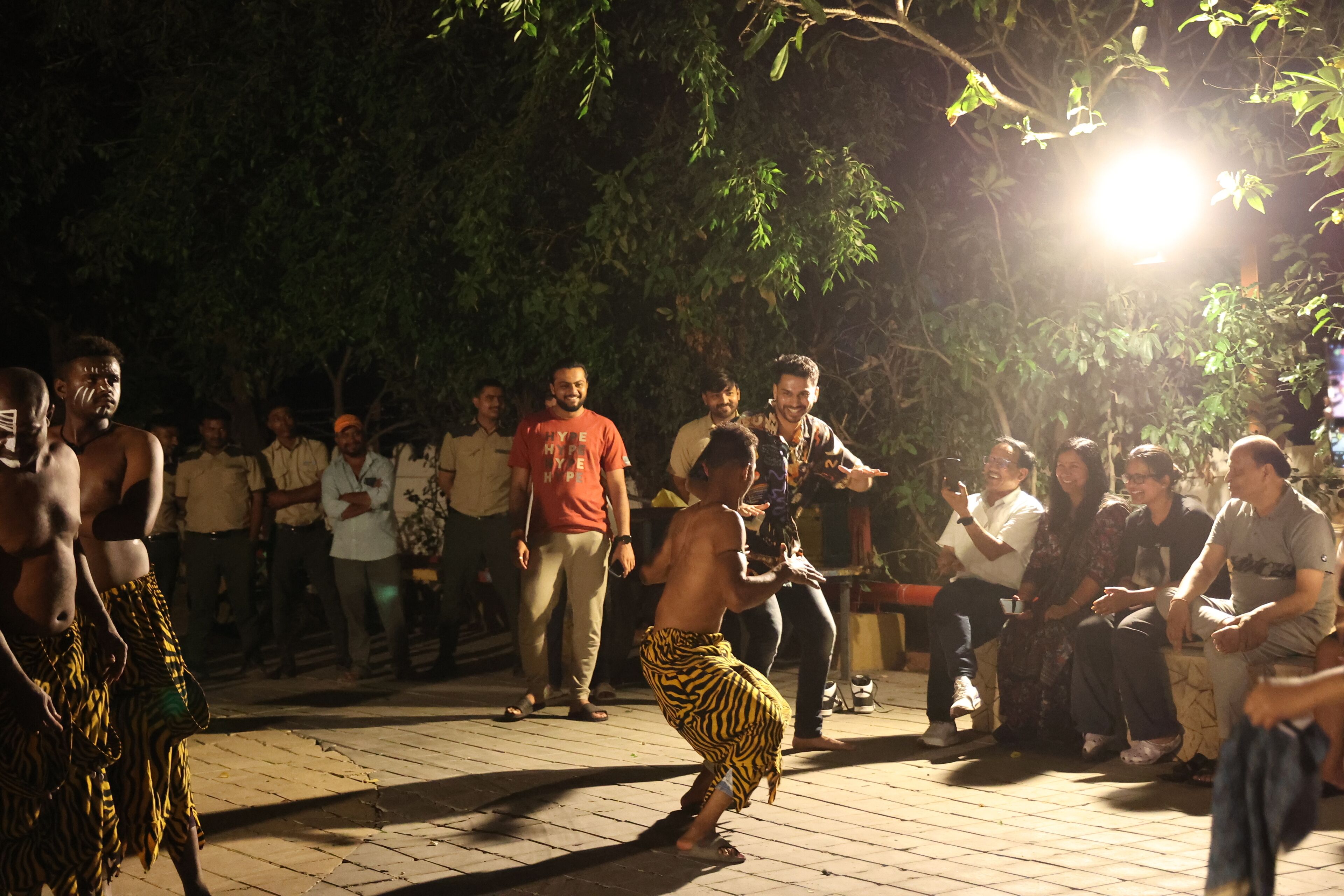 A group of people gathered outdoors at night, some standing and some seated, under a bright light source.