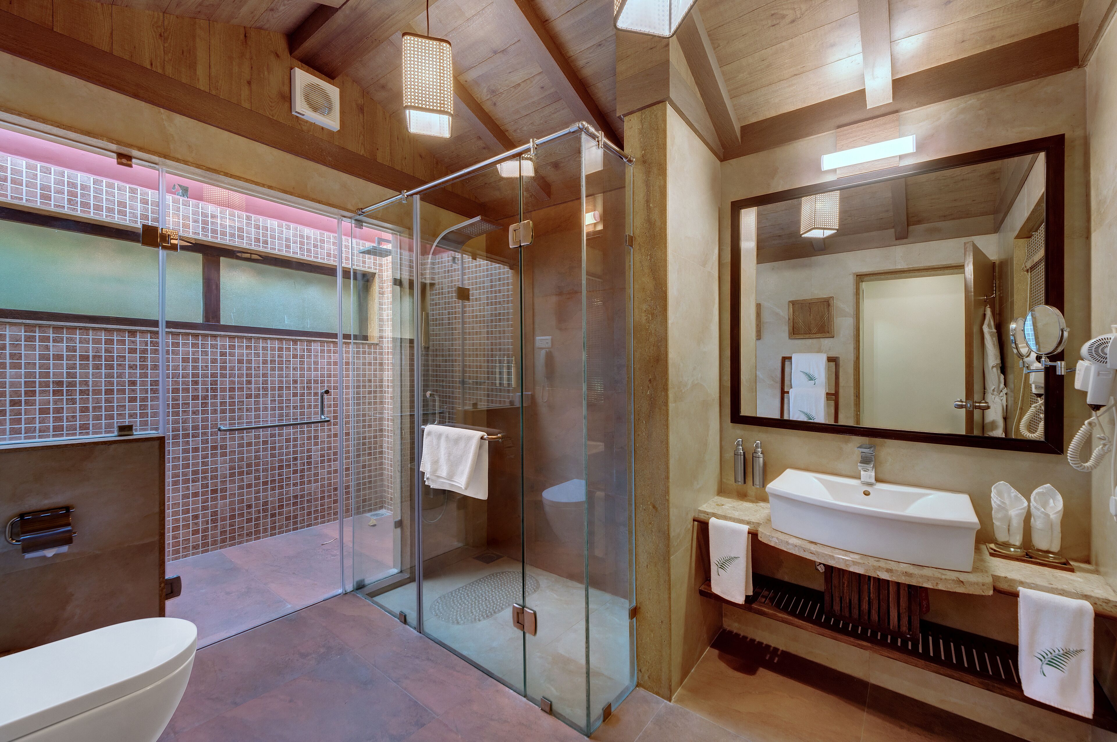 Un baño moderno con ducha de vidrio, un espejo grande y un lavamanos blanco.