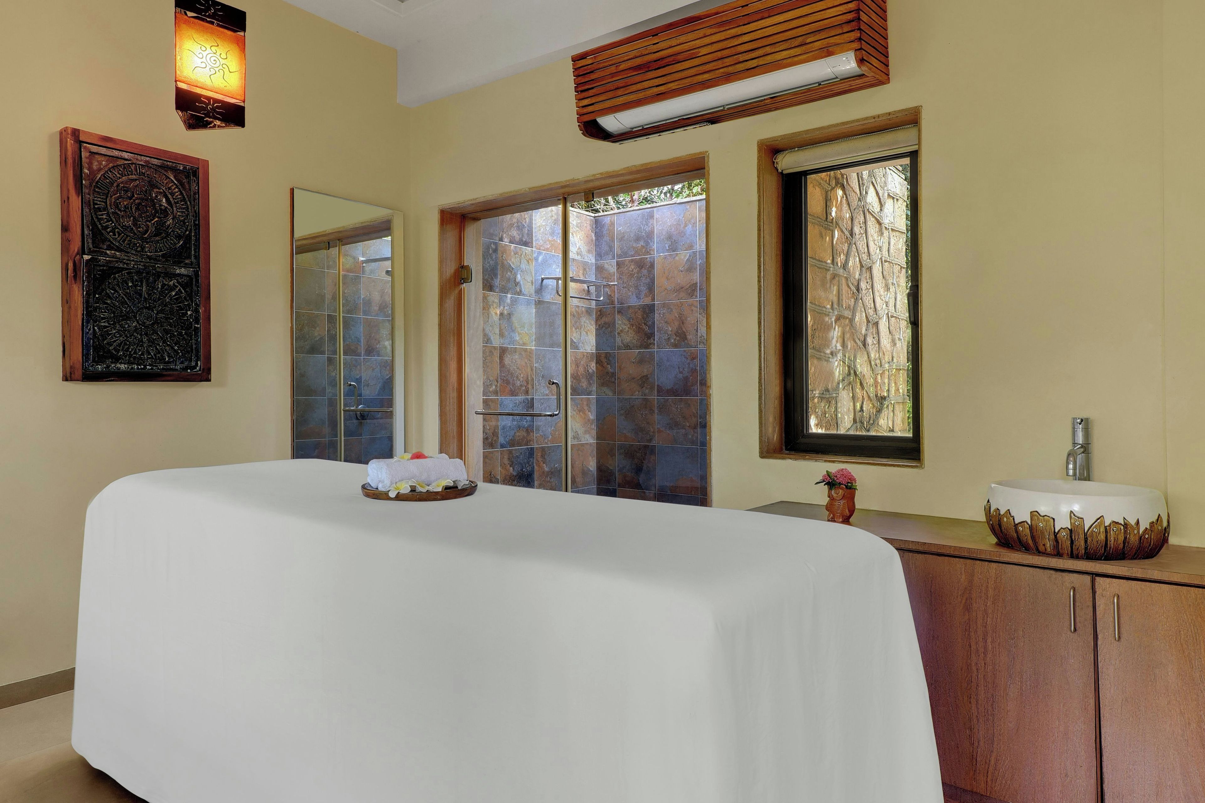 A hotel room with a large bed, a bathroom with a sink and mirror, and a window with a view of trees.