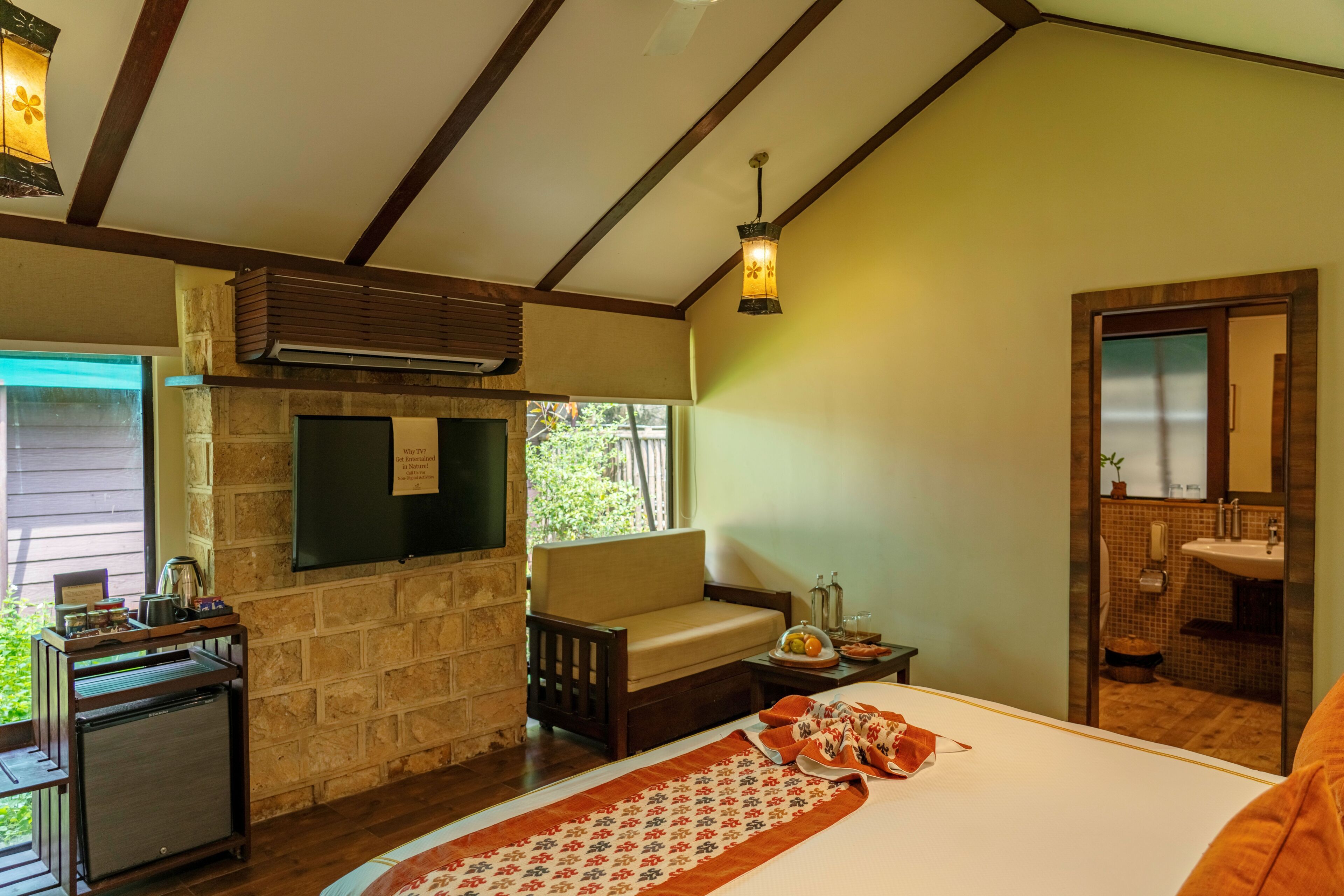 Quarto com cama, mesa pequena, cadeira, lareira, janela e banheiro visível através de uma porta de vidro.