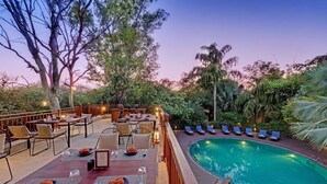 Un espace extérieur aménagé pour les repas, avec des tables et des chaises, une piscine et des chaises longues.