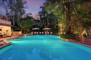 A swimming pool with lounge chairs and umbrellas, surrounded by trees and a building with a stone facade. - The Fern Gir Forest Resort Sasan Gir, Series by Marriott (Mendarda)