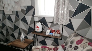 Una habitación acogedora con un sofá estampado, una pequeña mesa de madera con una tetera y tazas, y una ventana con cortinas.