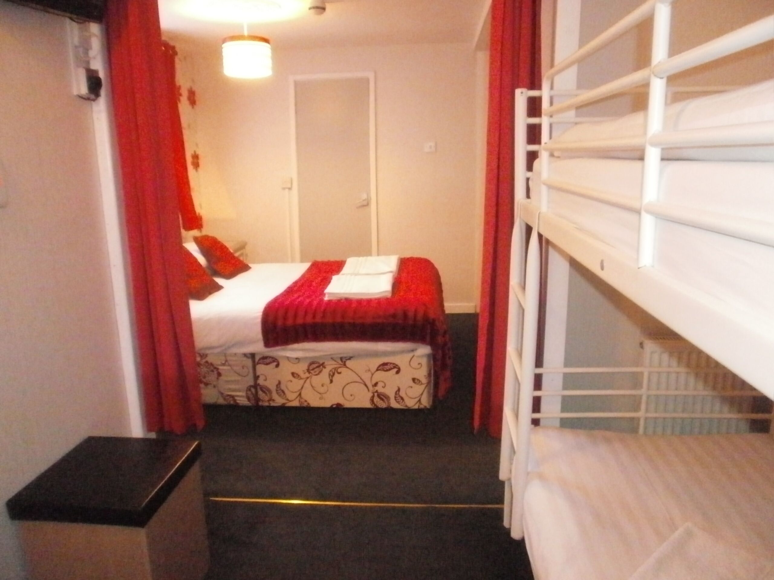Une chambre d’hôtel étroite, avec un lit, un petit bureau et une fenêtre à cadre blanc.