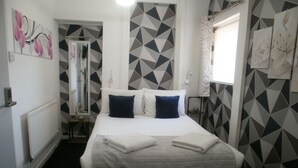 Un dormitorio con cama, almohadas, un radiador, una ventana y paredes con un estampado geométrico.
