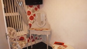 Una habitación de esquina con una silla blanca, una mesita con un espejo y un televisor en la pared.