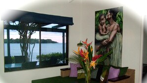 Una habitación con vistas al agua, un sofá de mimbre, una mesita con un florero y un cuadro en la pared.