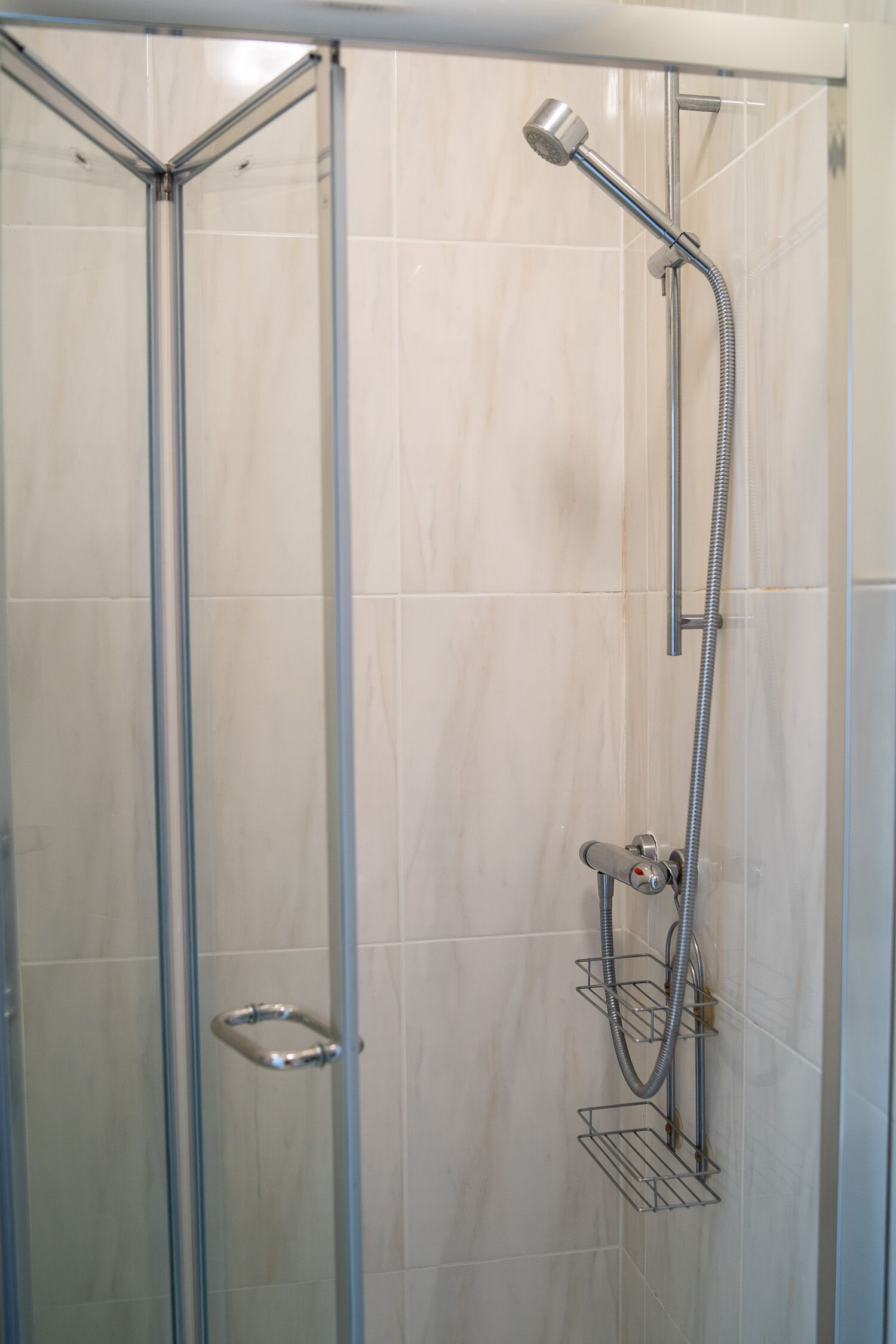 Ducha con cerramiento de vidrio, cabezal de ducha de mano y grifo empotrado.