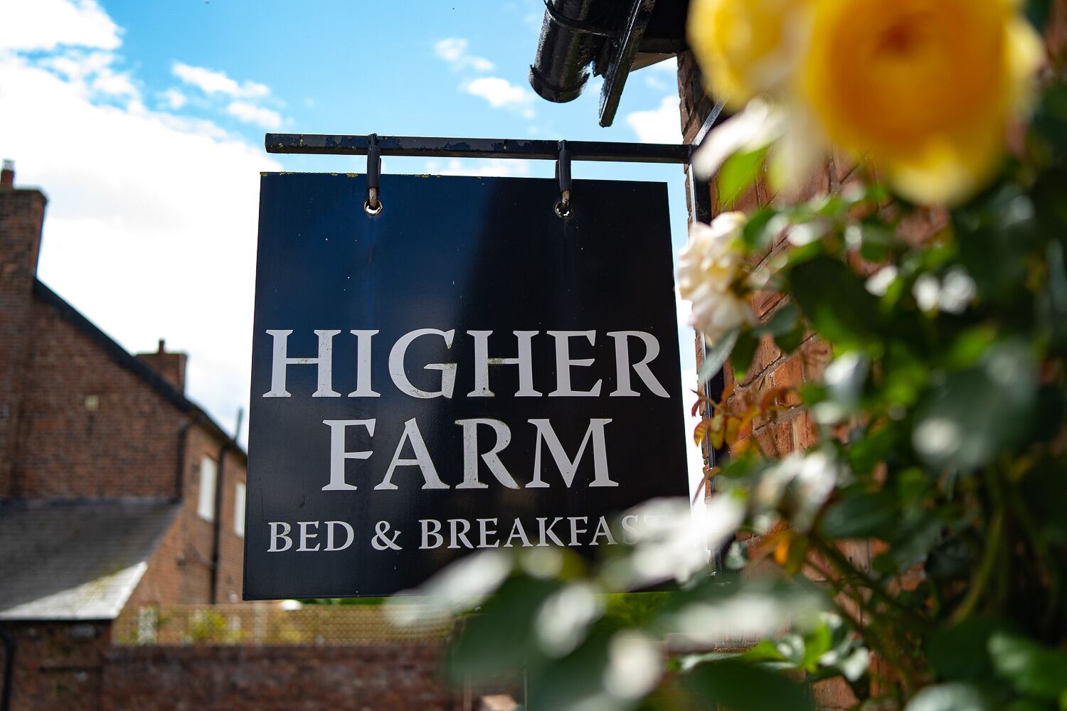 Een bord met daarop 'Higher Farm Bed & Breakfast', met een goed zicht op de tekst en een bakstenen gebouw op de achtergrond.