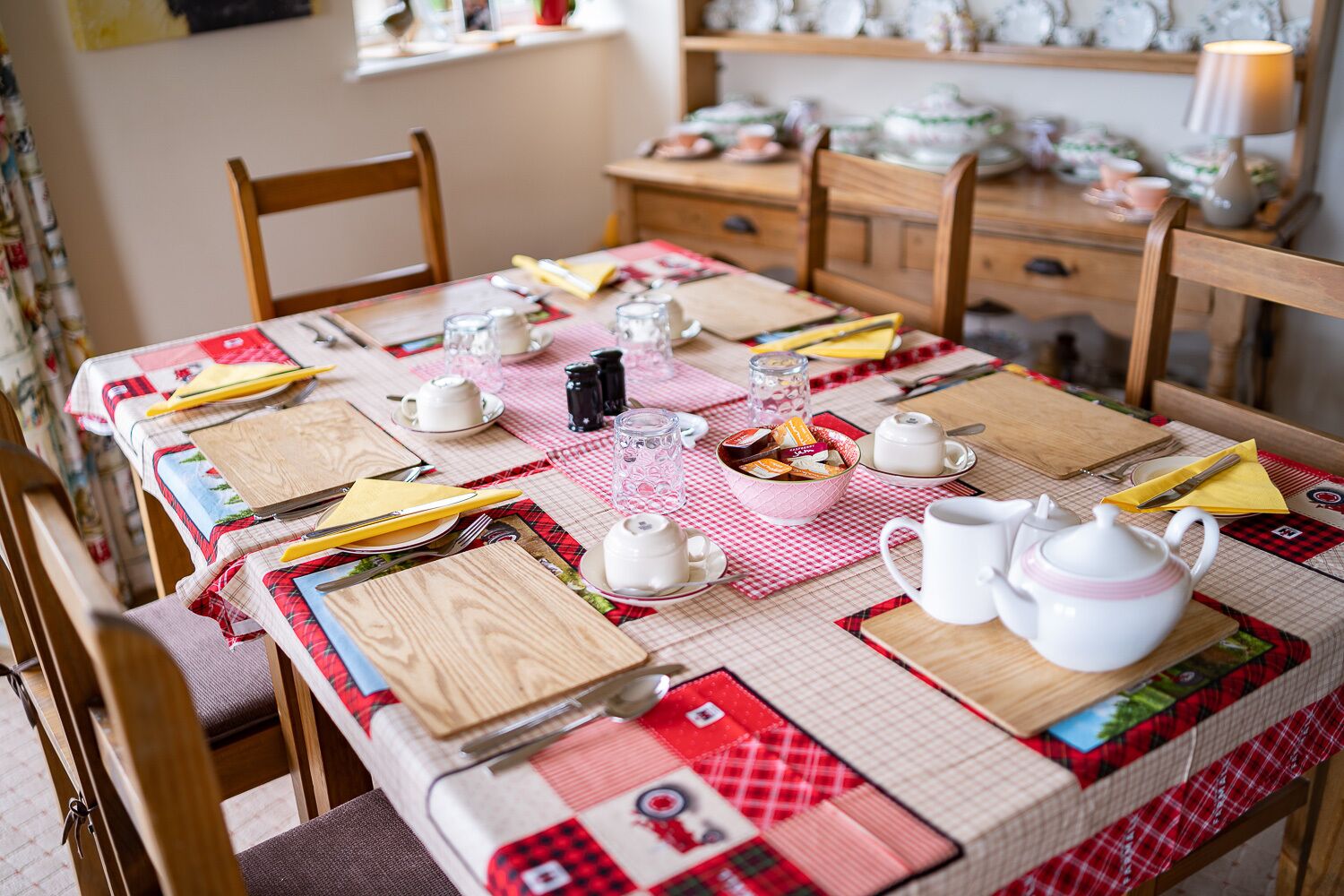 Een eettafel gedekt met theekoppen, theepotten en een schaal koekjes.