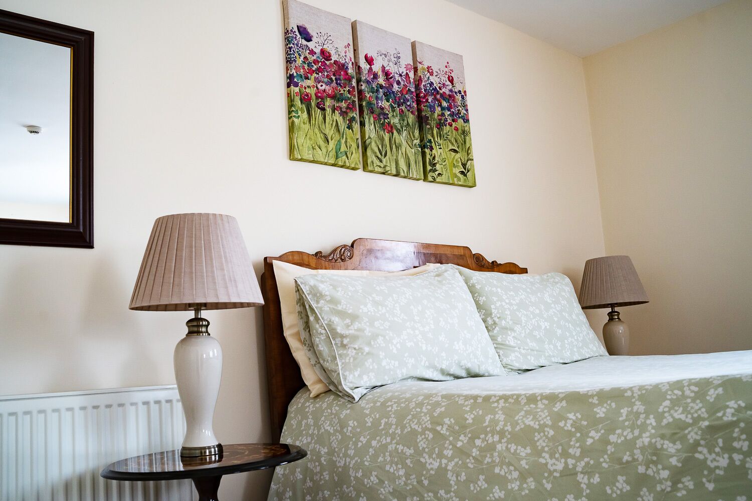 Habitación de hotel con una cama, dos lámparas de noche, un cabecero de madera y un cuadro floral en la pared.