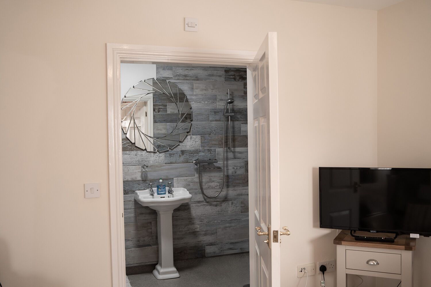 A bathroom with a pedestal sink, a shower, and a television on a wooden stand.