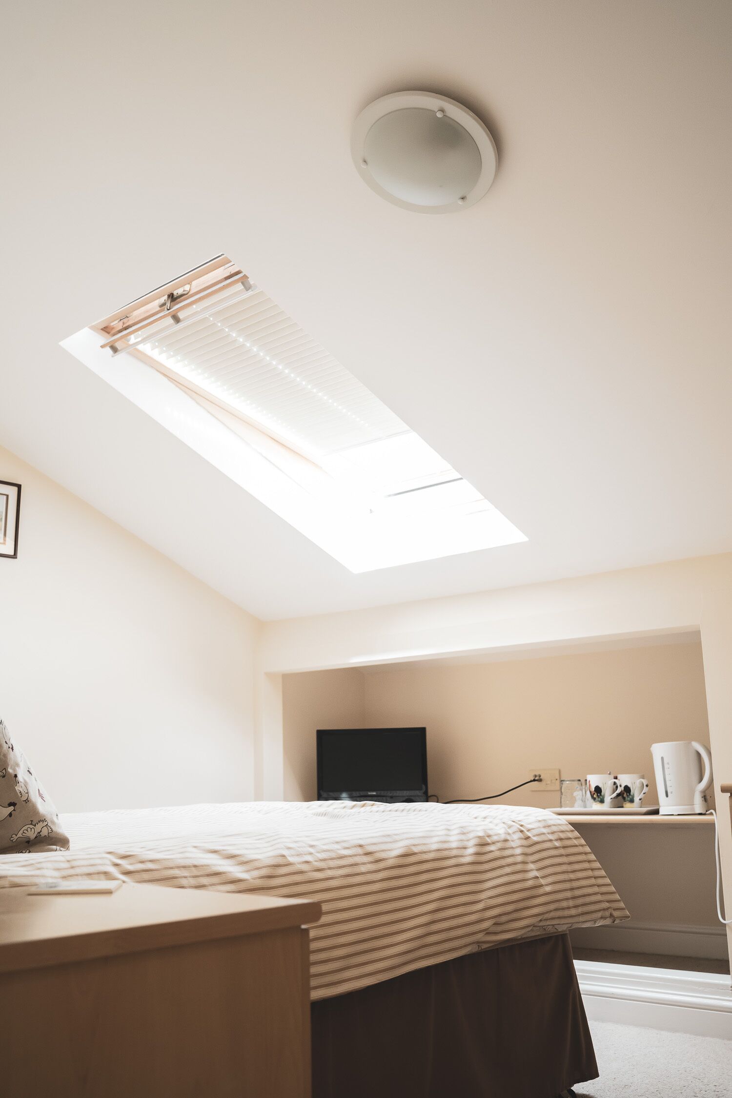 A bedroom with a skylight, a bed, a bedside table, a TV, and a coffee maker.
