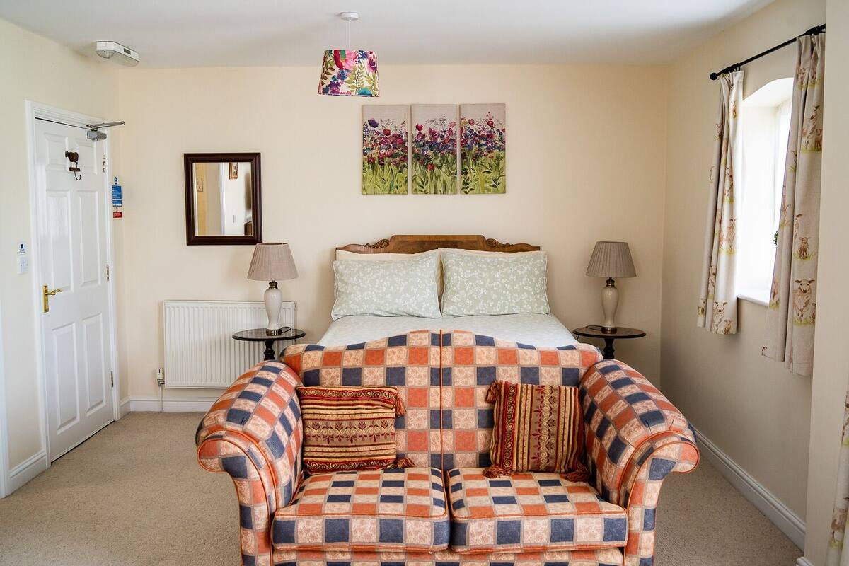 Un dormitorio con una cama, dos mesitas de noche, un sofá, un radiador, un espejo y una obra de arte floral en la pared.