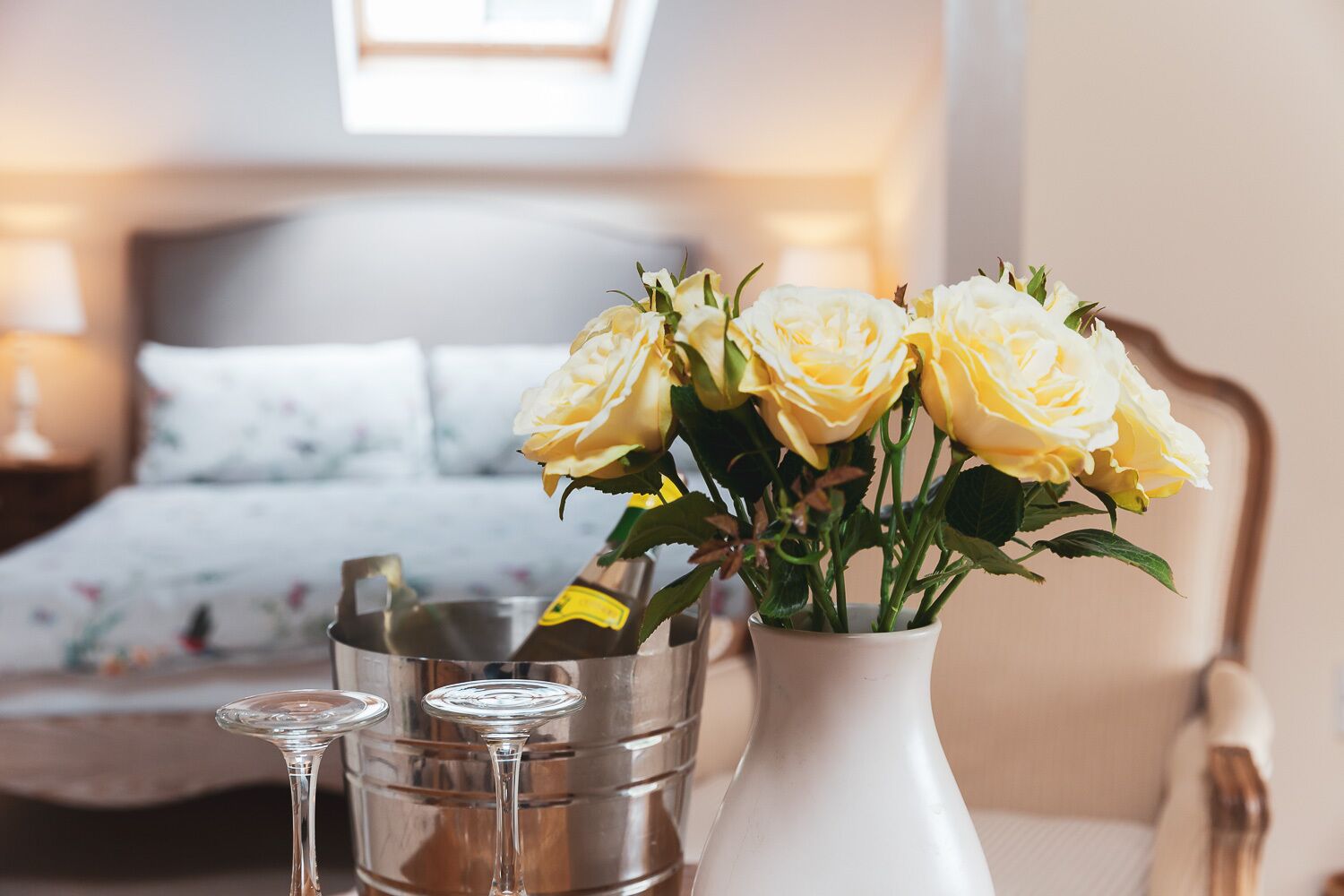 Ein Schlafzimmer mit einem Bett, einem Nachttisch mit einer Vase voller gelber Rosen und einem Metallbehälter.