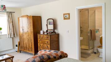 Un dormitorio con cama, armario de madera, cómoda, espejo, ventana con cortinas y baño con ducha e inodoro.